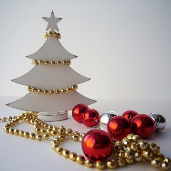 silueta de árbol de navidad blanco hecho en madera y con estrella arriba en la punta decorado con tira de bolitas doradas