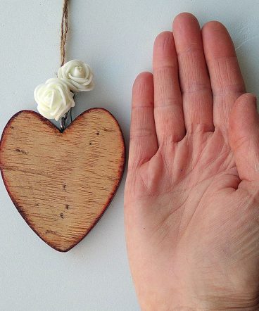 palma de la mano sobre superficie blanca con corazón de madera envejecido al lado