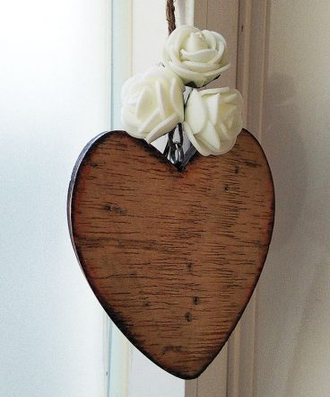 corazón de madera envejecido con tres flores pequeñas blancas en la parte superior sobre fondo blanco