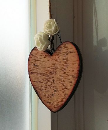 corazón de madera envejecido con tres flores pequeñas blancas en la parte superior sobre fondo blanco