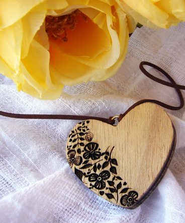 colgante con forma de corazón hecho en madera y con con flores grabadas en la mitad izquierda