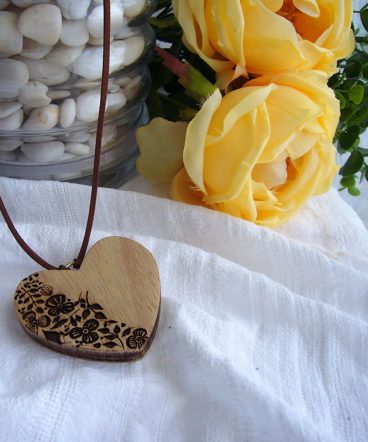 corazón de madera grabado con flore en su parte izquierda sobre superficie blanca con rosas amarillas al fondo