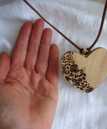 palma de una mano sobre superficie blanca al lado de corazón de madera grabado en su parte izquierda con flores
