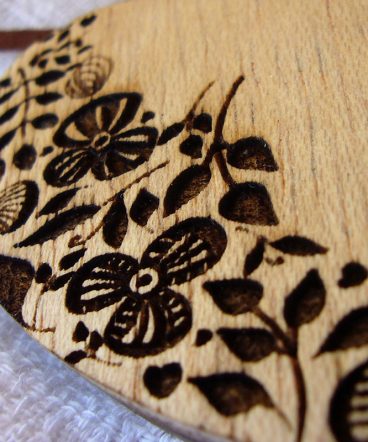 detalle de flores grabadas en un colgante con forma de corazón hecho en madera