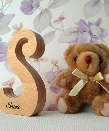 Letra S de madera personalizada con el nombre de Saioa sobre fondo con flores malva y osito de peluche a la derecha