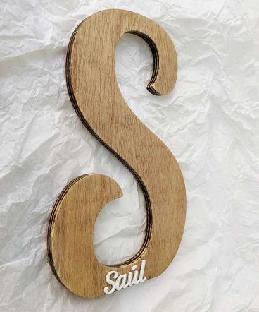 letra S de madera vista de lado sobre papel blanco arrugado decorada con el nombre de Saúl en blanco y en relieve pegado en la parte de abajo