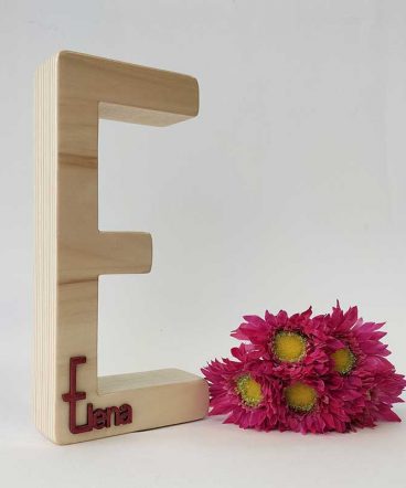 fondo blanco con letra e de madera maciza con el nombre de Elena en rojo en relieve pegado en la parte de abajo y flores fucsia a la derecha