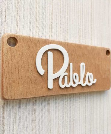 pared de rayas beiges y grises con tablero de madera rectangular con el nombre de Pablo color blanco y en relieve pegado en el centro