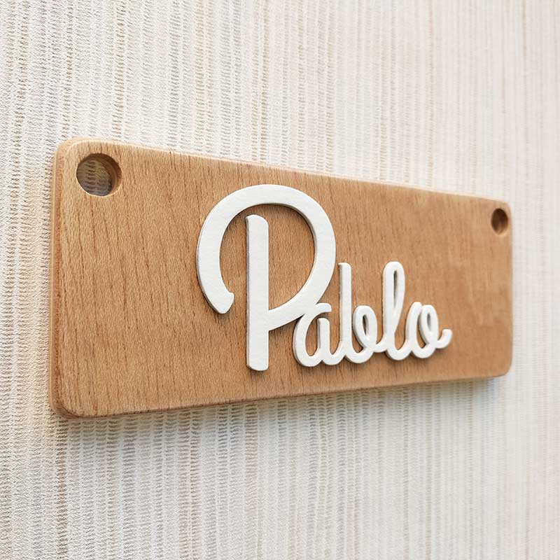 pared de rayas beiges y grises con tablero de madera rectangular con el nombre de Pablo color blanco y en relieve pegado en el centro
