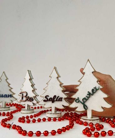 mano detrás de cuatro árboles de navidad blancos personalizados con nombres en relieve