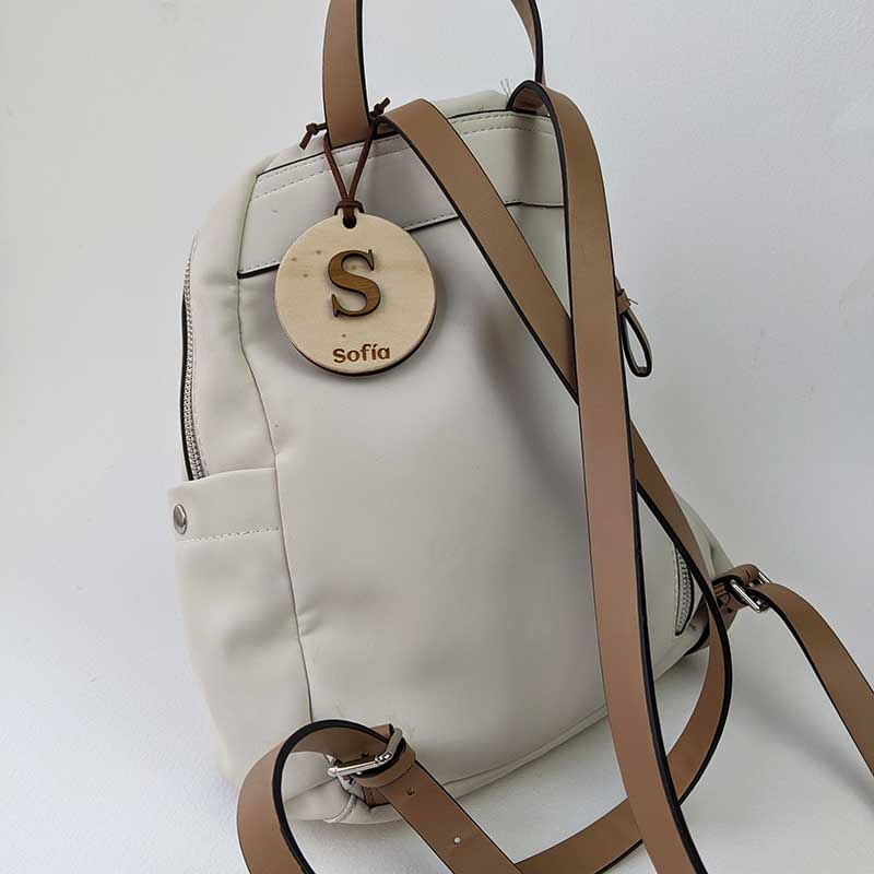 mochila blanca con colgante redondo de madera personalizado con letra y grabado