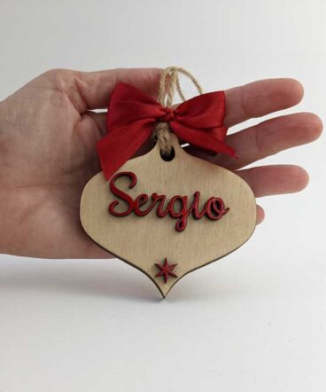 mano sujetando lágrima de navidad de madera con el nombre de Sergio y una estrella roja