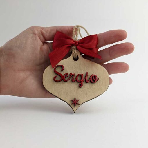 mano sujetando lágrima de navidad de madera con el nombre de Sergio y una estrella roja