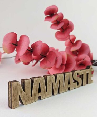 palabra namasté de madera envejecida sobre fondo blanco y flores rojas detrás