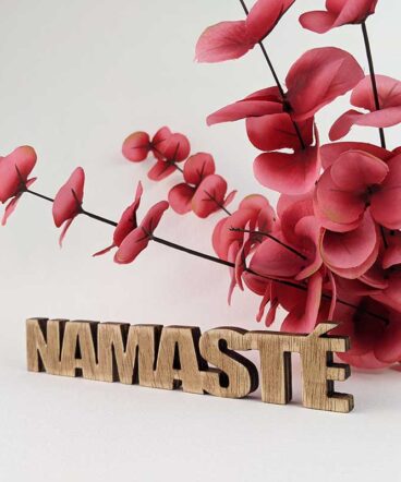 palabra namasté de madera envejecida sobre fondo blanco y flores rojas detrás