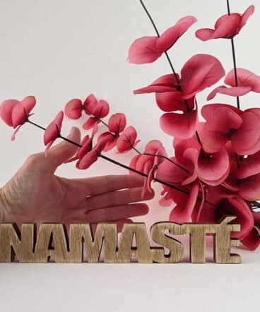palabra namasté de madera envejecida sobre fondo blanco, mano para comparar tamaño y flores rojas