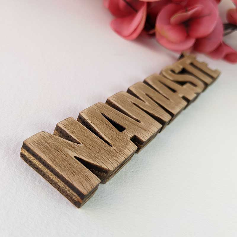 detalle palabra namasté de madera envejecida sobre fondo blanco y flores rojas detrás