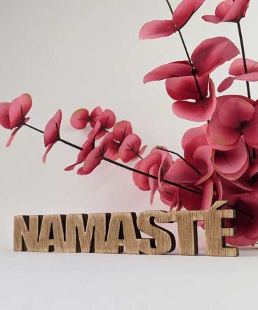 palabra namasté de madera envejecida sobre fondo blanco y flores rojas detrás
