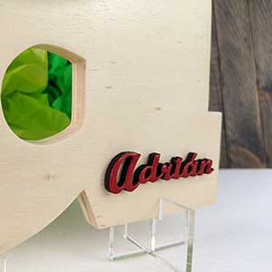 Detalle de letra a de madera natural con el nombre de Adrián color rojo y en relieve en la parte de abajo