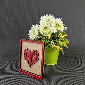 cuadrito con el fondo de madera, con la palabra amor en el centro color rojo y forma de corazón