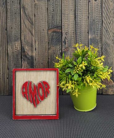 cuadrito con el fondo de maderac on la palabra amor en el centro con forma de corazón, en relieve y en color rojo