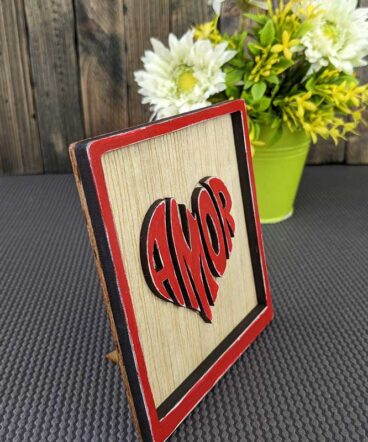 cuadrito de madera con marco y la palabra amor color rojo en el centro,en relieve y con forma de corazón