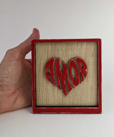 detalle de cuadrito de madera con la palabra amor en el centro con forma de corazón, en relieve y en color rojo