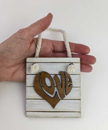 mano sujetando cuadrito blanco con la palabra LOVE con forma de corazón hecha de roble