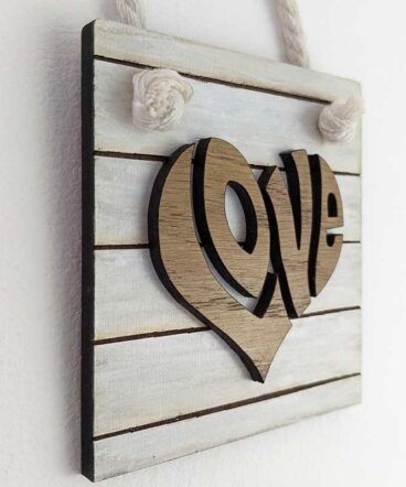 Pequeño tablero color blanco sucio con la palabra LOVE de roble pegada en el centro en relieve y con forma de corazón hecha en roble natural