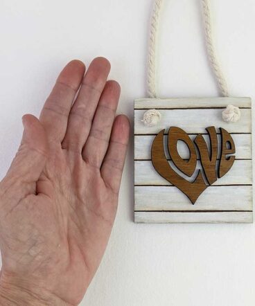Pequeño tablero color blanco sucio con la palabra LOVE de roble en el centro en relieve y con forma de corazón
