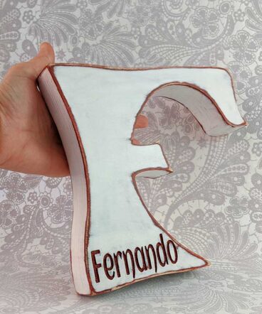 letra F color blanco sujeta por una mano con bordes burdeos y nombre Fernando en burdeos