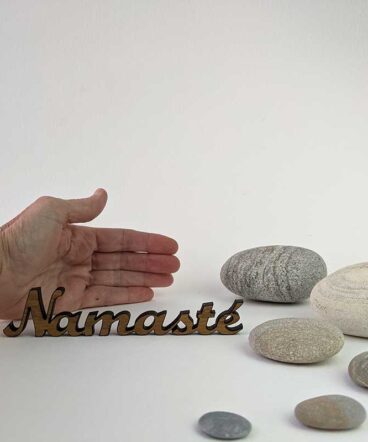 palabra namasté de roble sobre fondo blanco con piedras redondeadas y grises y una mano para saber tamaño