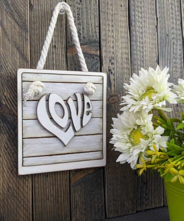 colgante cuadrado blanco roto con la palabra LOVE en el centro en relieve y con forma de corazón pintada en blanco vintage