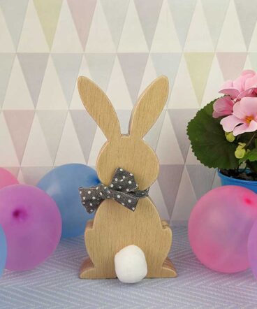 fondo en tonos grisáceos on globos de colores a los lados y silueta de madera de conejo de pascua con lazo gris con moña en el cuello