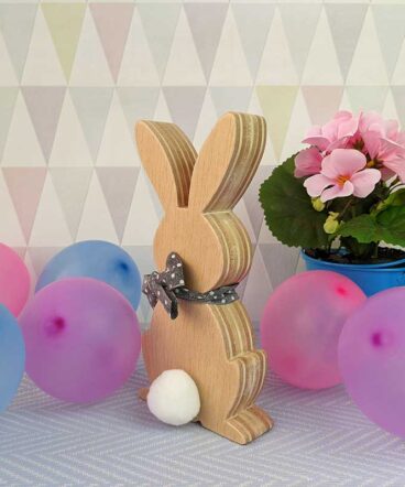 fondo en tonos grises con globos de colores y flores rosas con conejo de pascua de madera delante