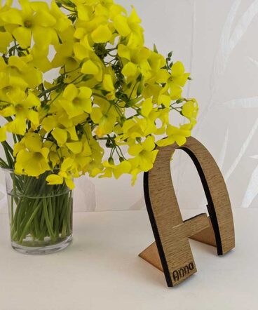 fondo blanco con vaso con flores amarillas y letra A de madera de roble con nombre Anna grabado