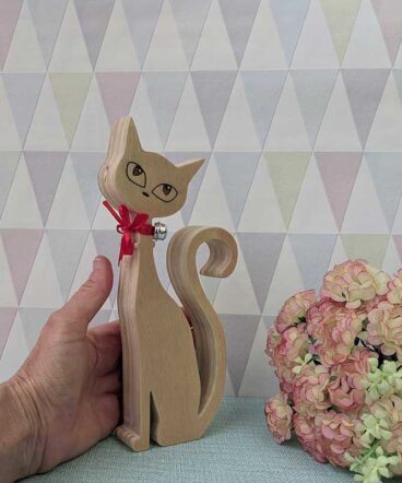 mano con silueta de gato de madera con los ojos grabados y lazo rojo