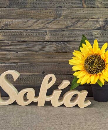 nombre de Sofía hecho en madera natural sobre fondo de tablas oscuras y flor amarilla al fondo