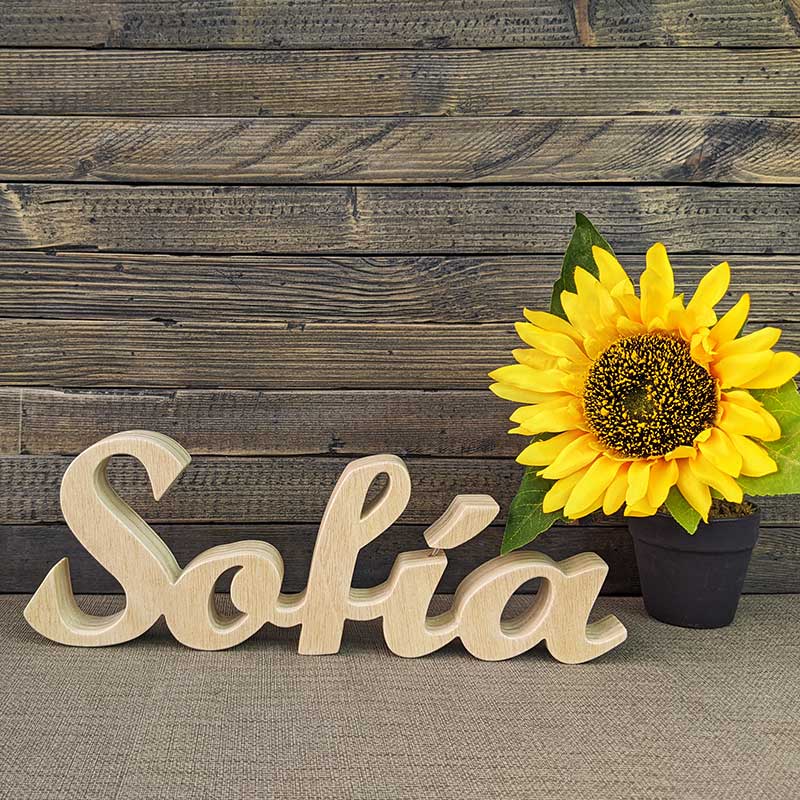 nombre de Sofía hecho en madera natural sobre fondo de tablas oscuras y flor amarilla al fondo