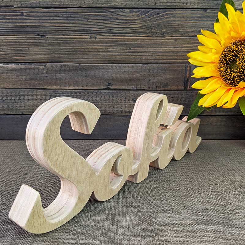 nombre Sofía hecho en madera natural sobre fondo de tablas oscuras y flor amarilla al fondo