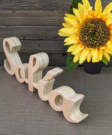 nombre de Sofía hecho en madera natural sobre fondo gris y flor amarilla al fondo