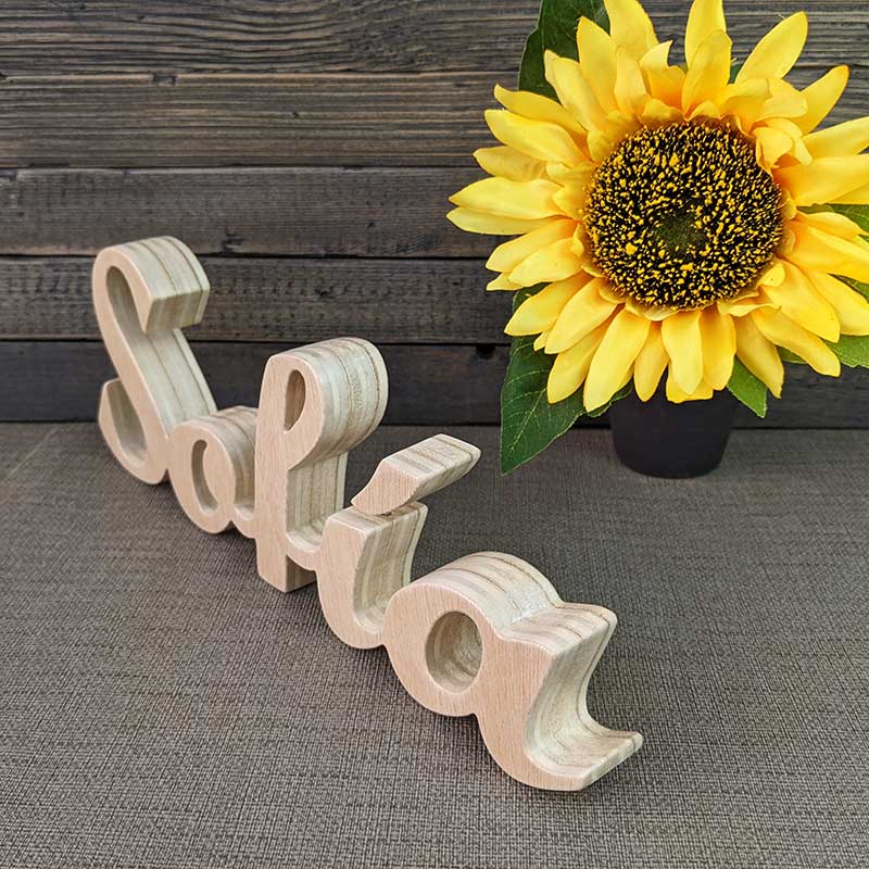 nombre de Sofía hecho en madera natural sobre fondo gris y flor amarilla al fondo